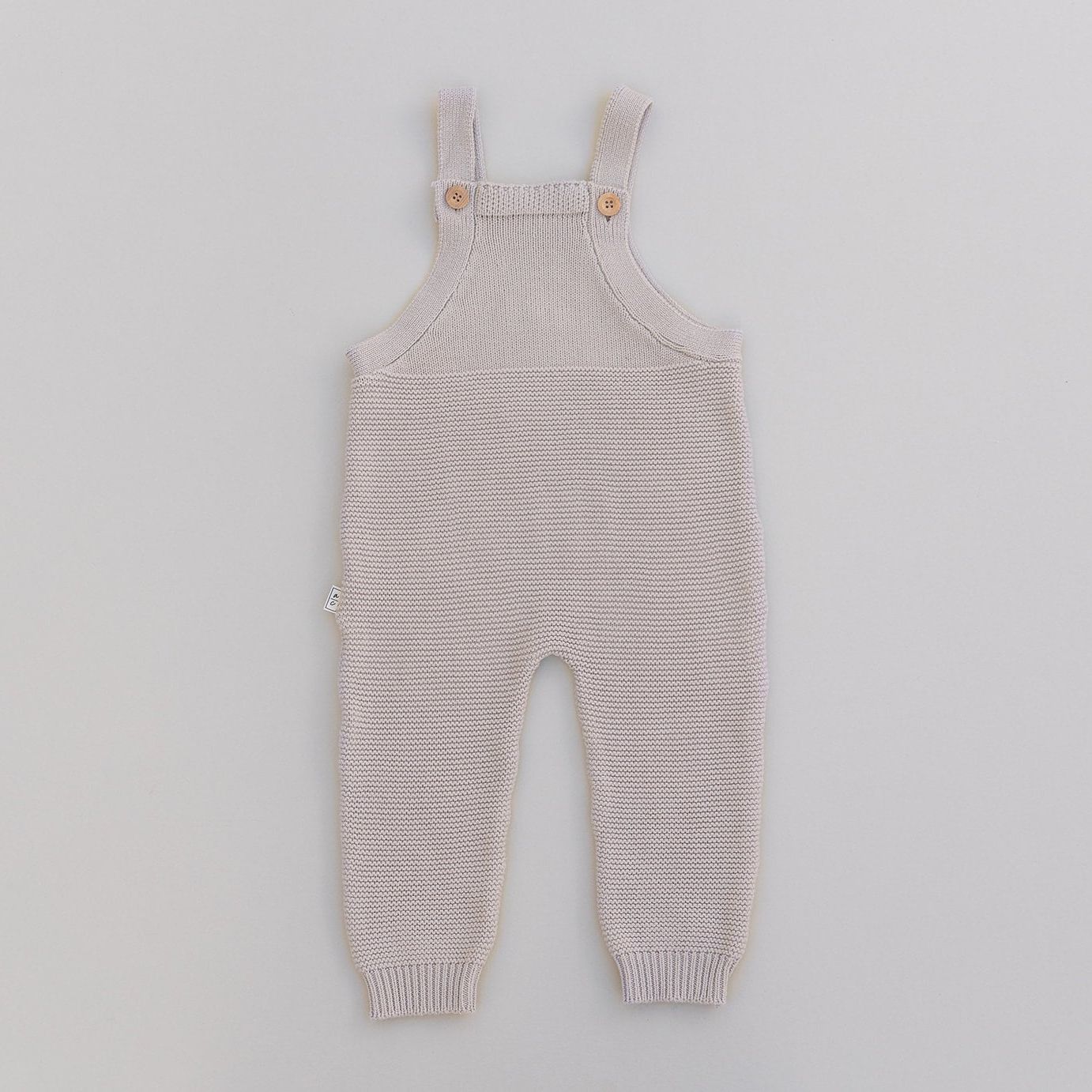 Knitted baby overalls in oat on a light gray background