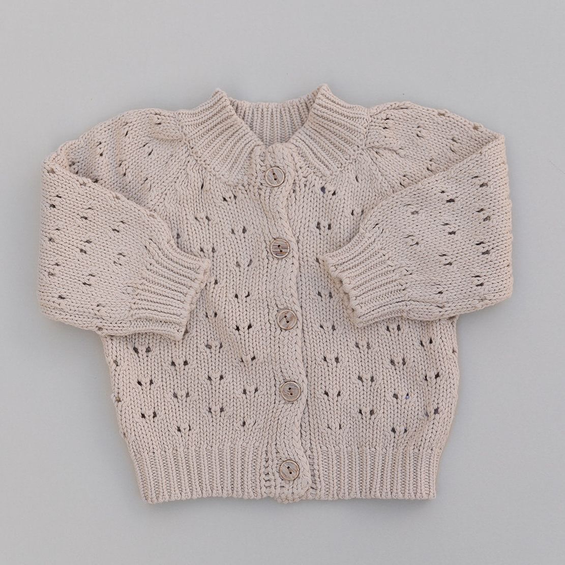 Chunky knitted baby sweater with button details on a gray background