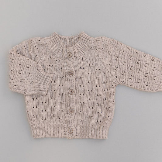 Knitted baby cardigan with buttons and with a subtle pattern on a gray background