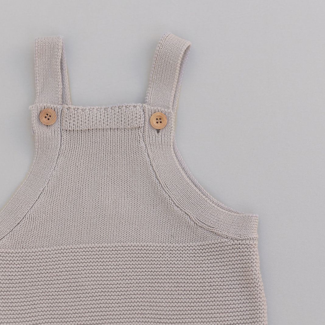 Knitted baby romper with button straps on a gray background