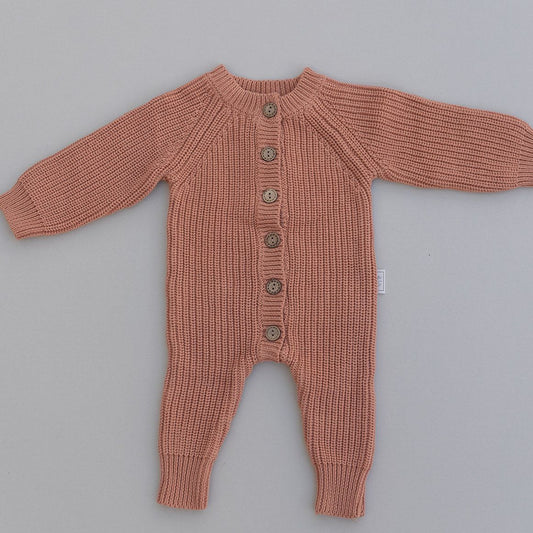 Rust colored baby romper with buttons on a gray background