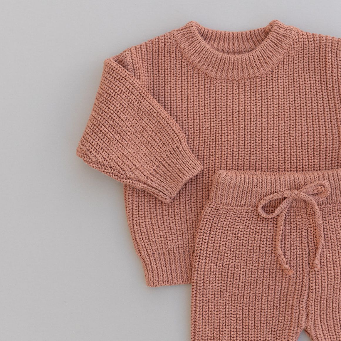 Knitted rust colored sweater and pants set on a light gray background
