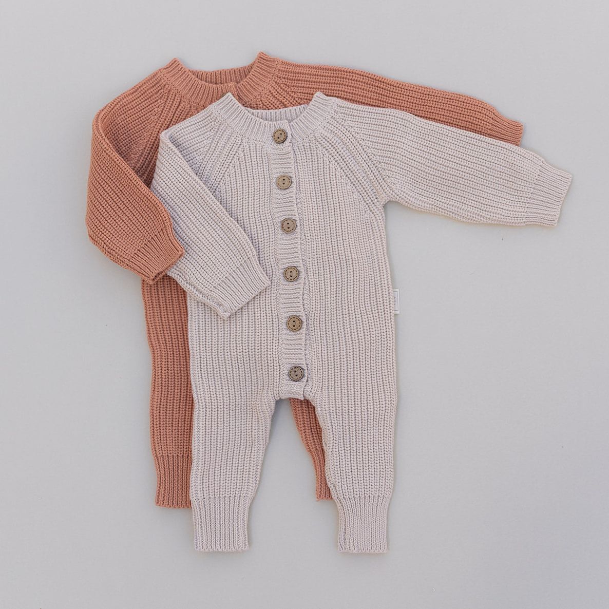 Two baby rompers, one rust and one cream, on a light gray background.