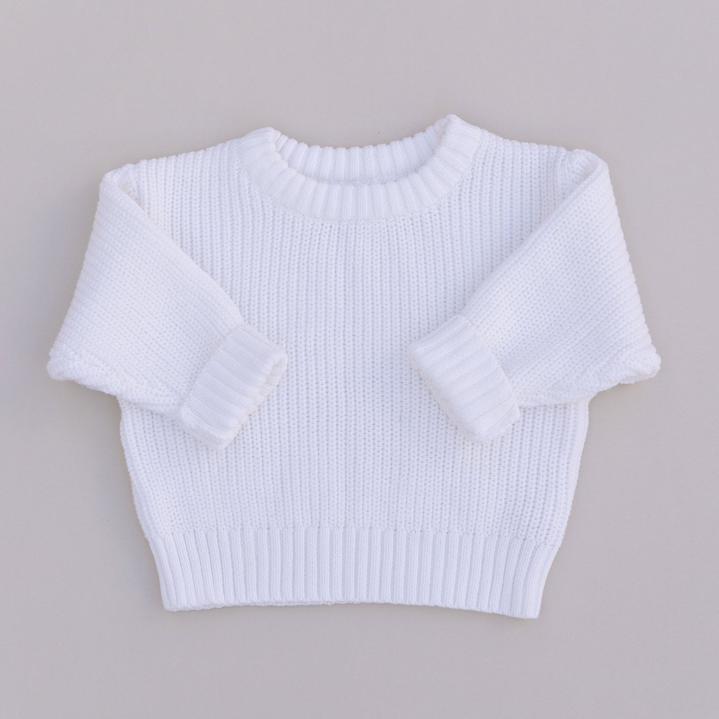 A white organic cotton knit sweater for babies, displayed against a white background.