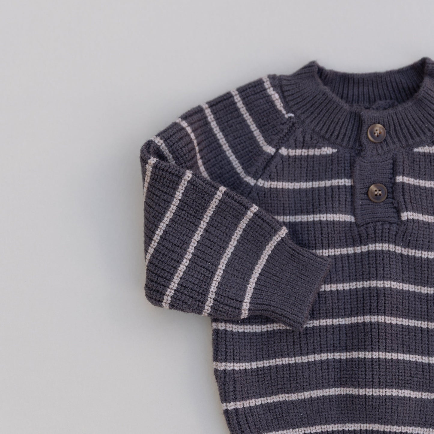 Striped knitted brown sweater with cream stripes and two buttons on a light gray background