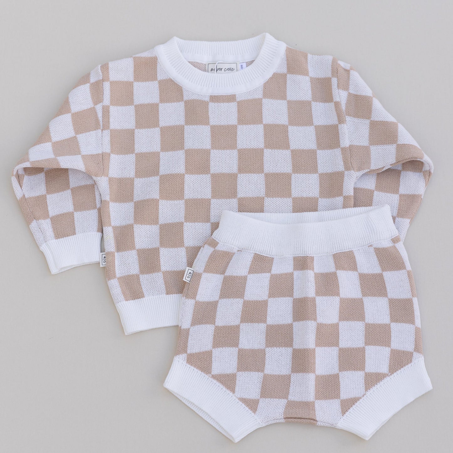 A two-piece baby outfit with a checkered long-sleeve sweater and matching bloomers in beige and white colors.