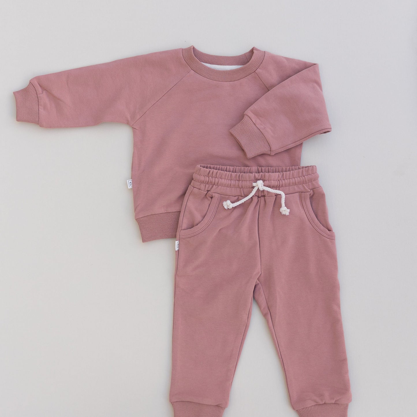 A baby jogger set in pink, including a long-sleeved top and matching pants, laid flat on a white background.