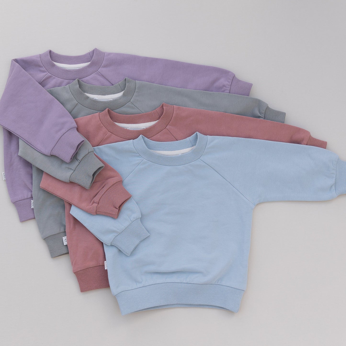 Stack of colorful sweatshirts in purple, green, pink, and blue on a gray background
