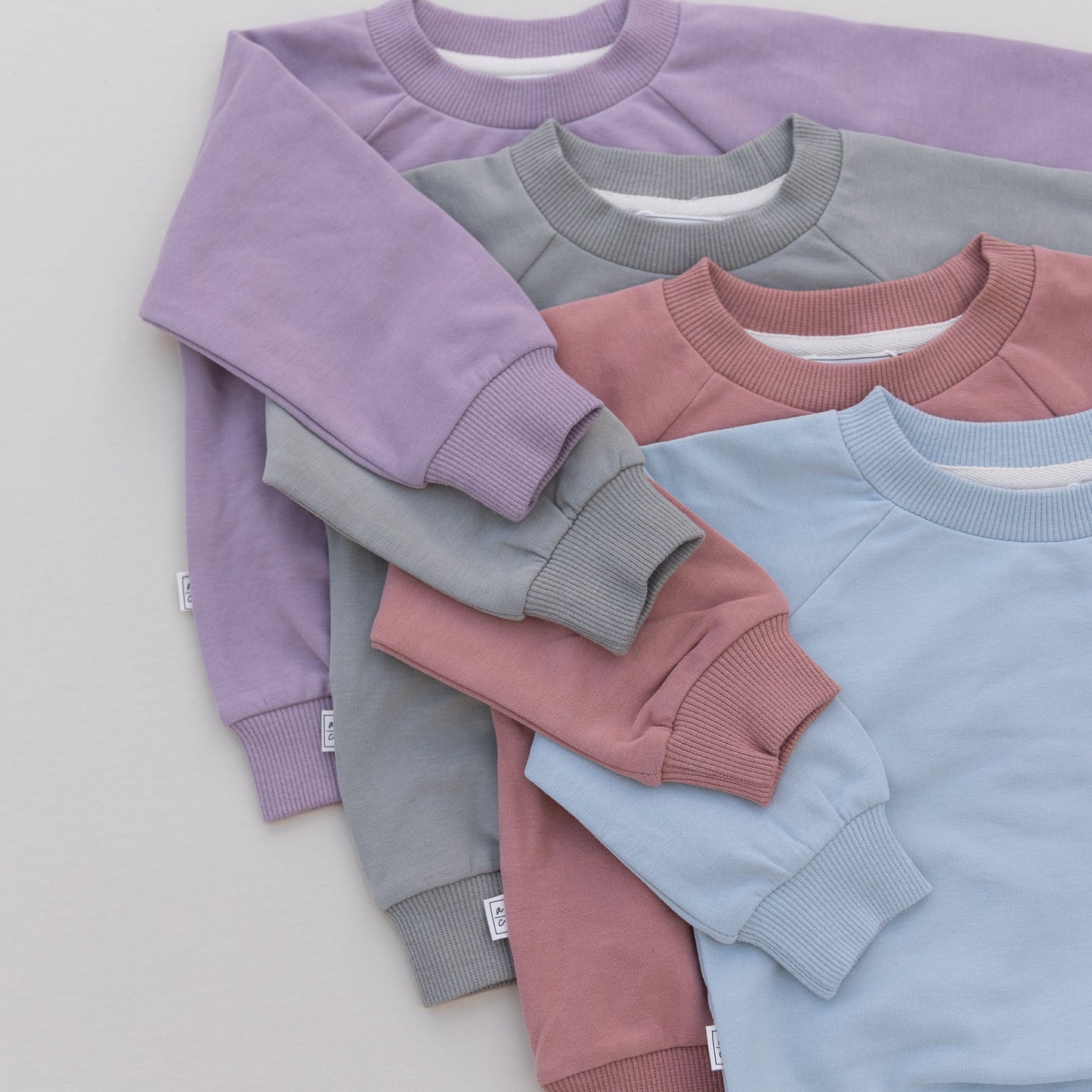 Stack of pastel-colored sweatshirts in purple, green, pink and blue on a light gray background