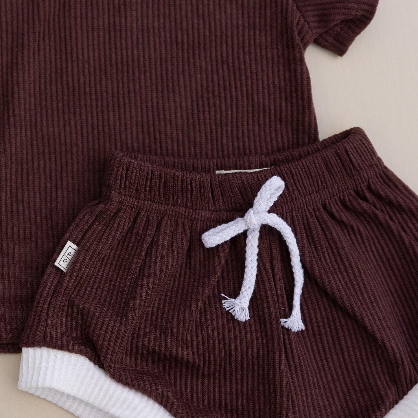 Brown ribbed outfit with shorts and a top with white trim on a light background