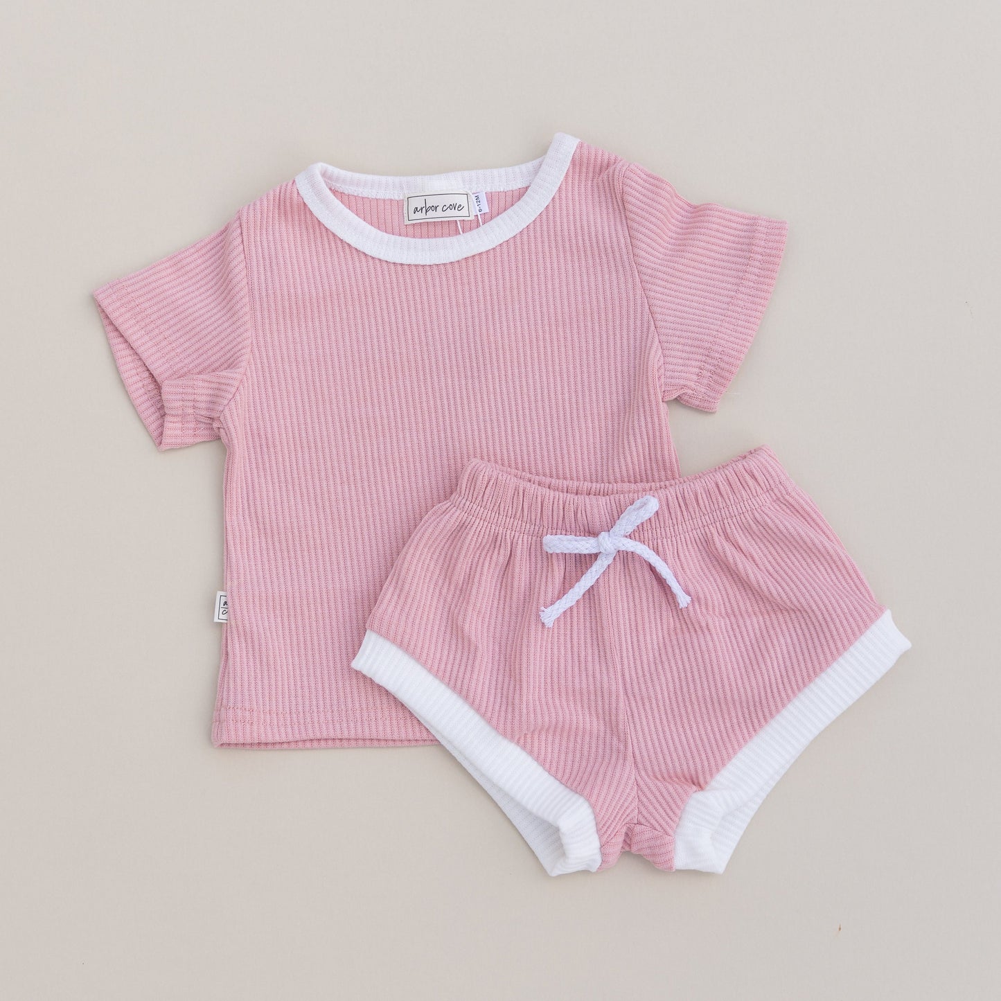 A set of children's clothing, consisting of a pink ribbed t-shirt and matching shorts with white contrast trim and a drawstring.