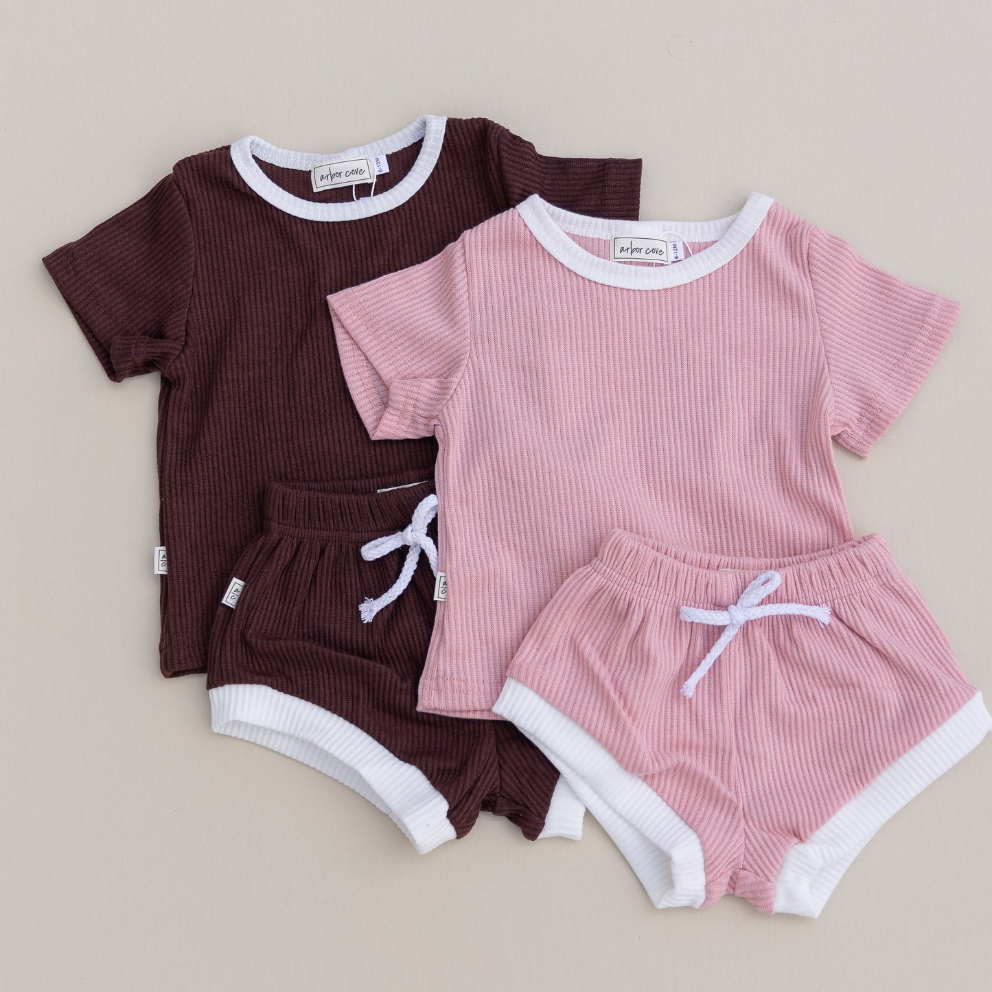 Two sets of children's clothing in brown and pink both with white trim on a beige background