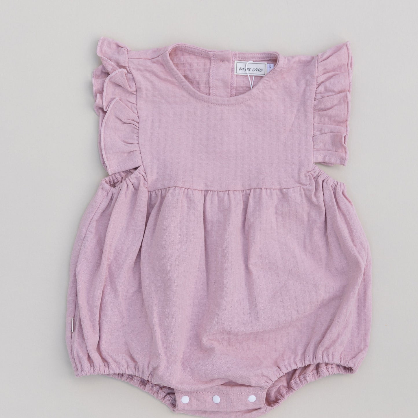 A pink ruffled bubble onesie with short sleeves and snap closures on the bottom for a baby.