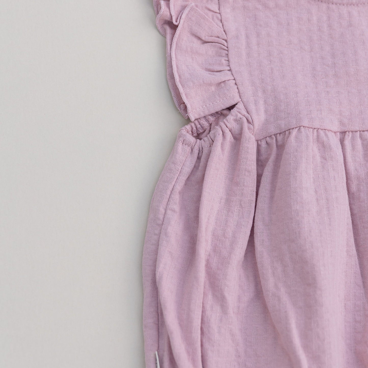 Pink baby bubble romper with ruffled sleeves on a light gray background