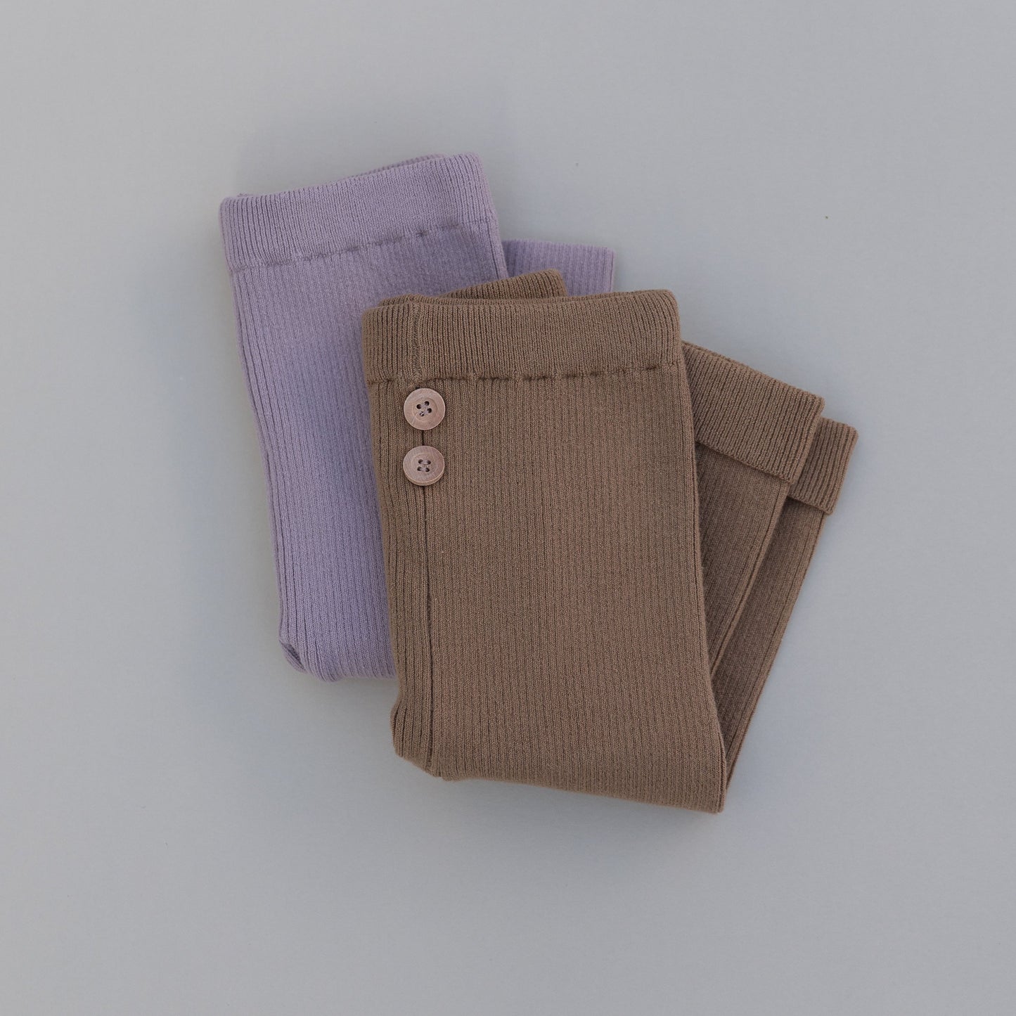Purple and brown ribbed baby leggings folded on a gray background