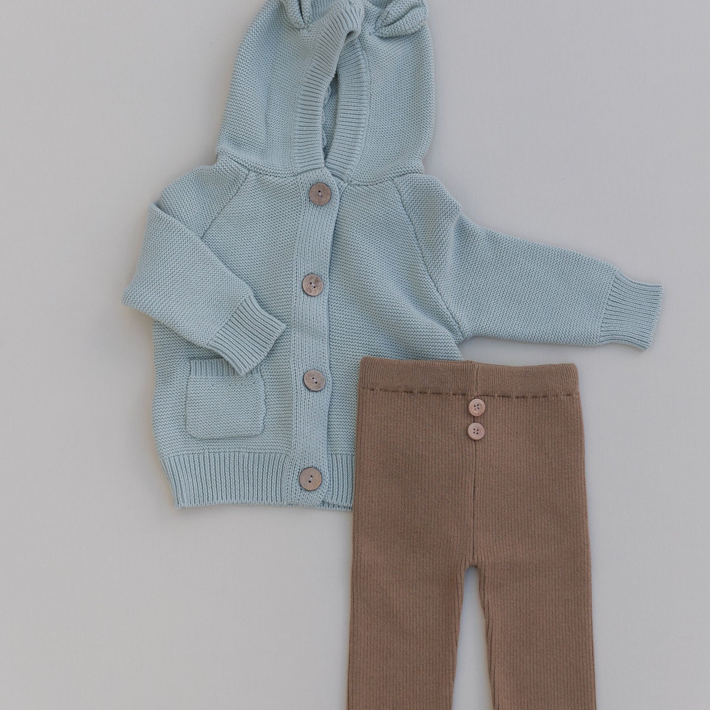 Baby bear knit cardigan in green paired with organic cotton brown baby pants with buttons on a cream background.
