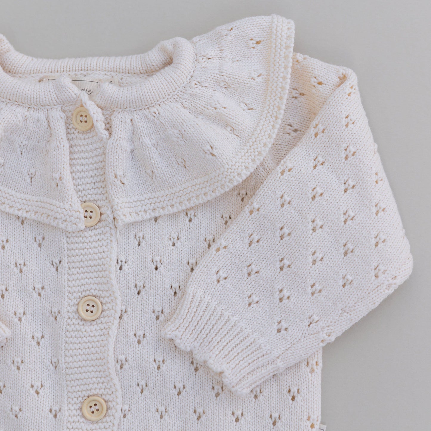 Cream knitted pointelle baby cardigan with buttons on a gray background