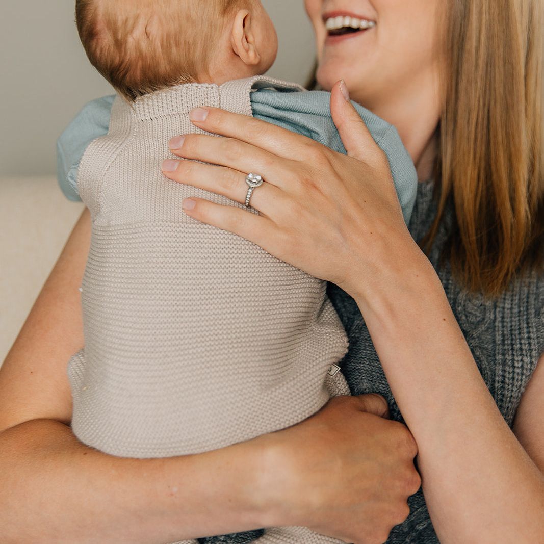 Woman holding a baby wearing a knit pair of baby overalls and smiling