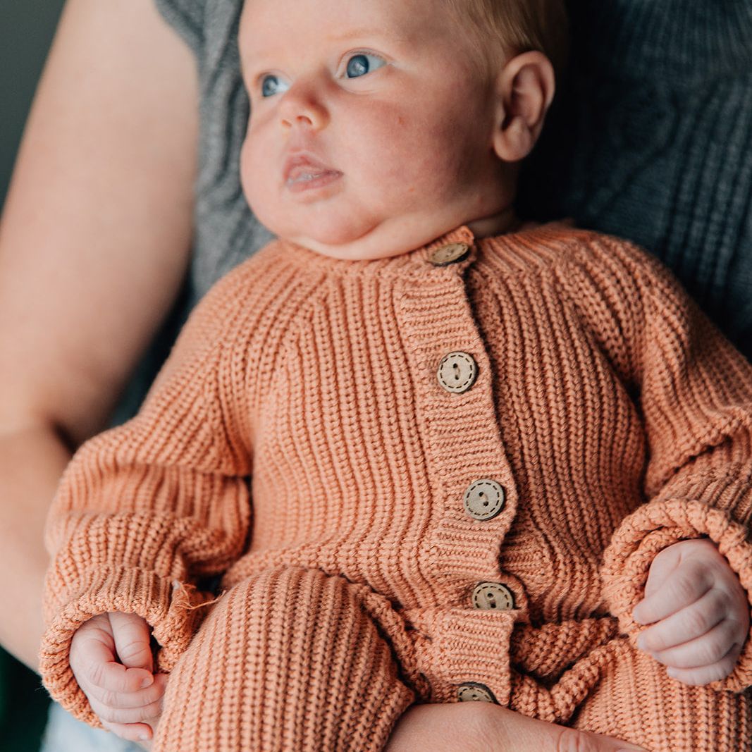 Baby in a knitted orange romper being held by an adult