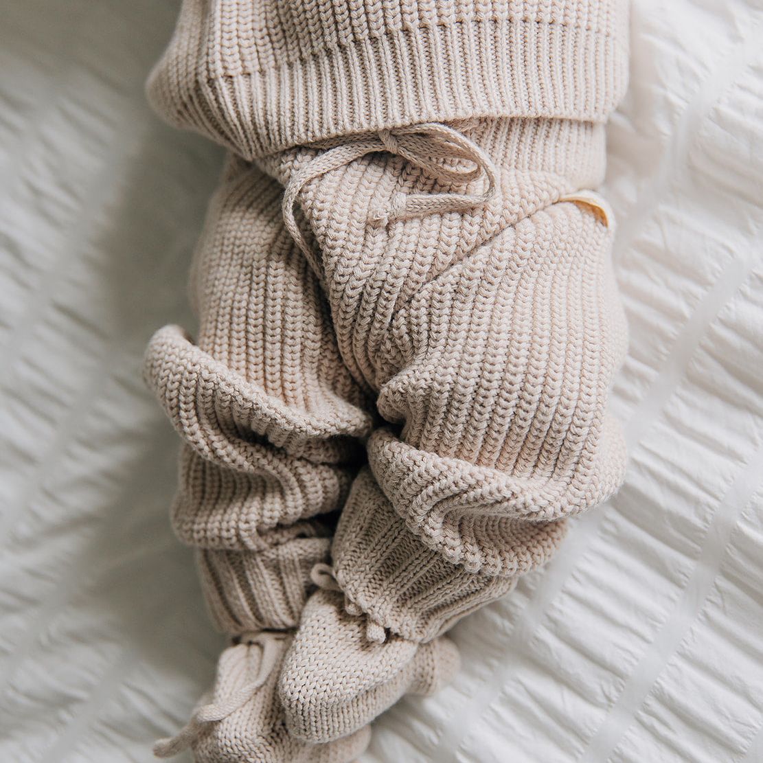 Beige knitted baby outfit on a white textured surface