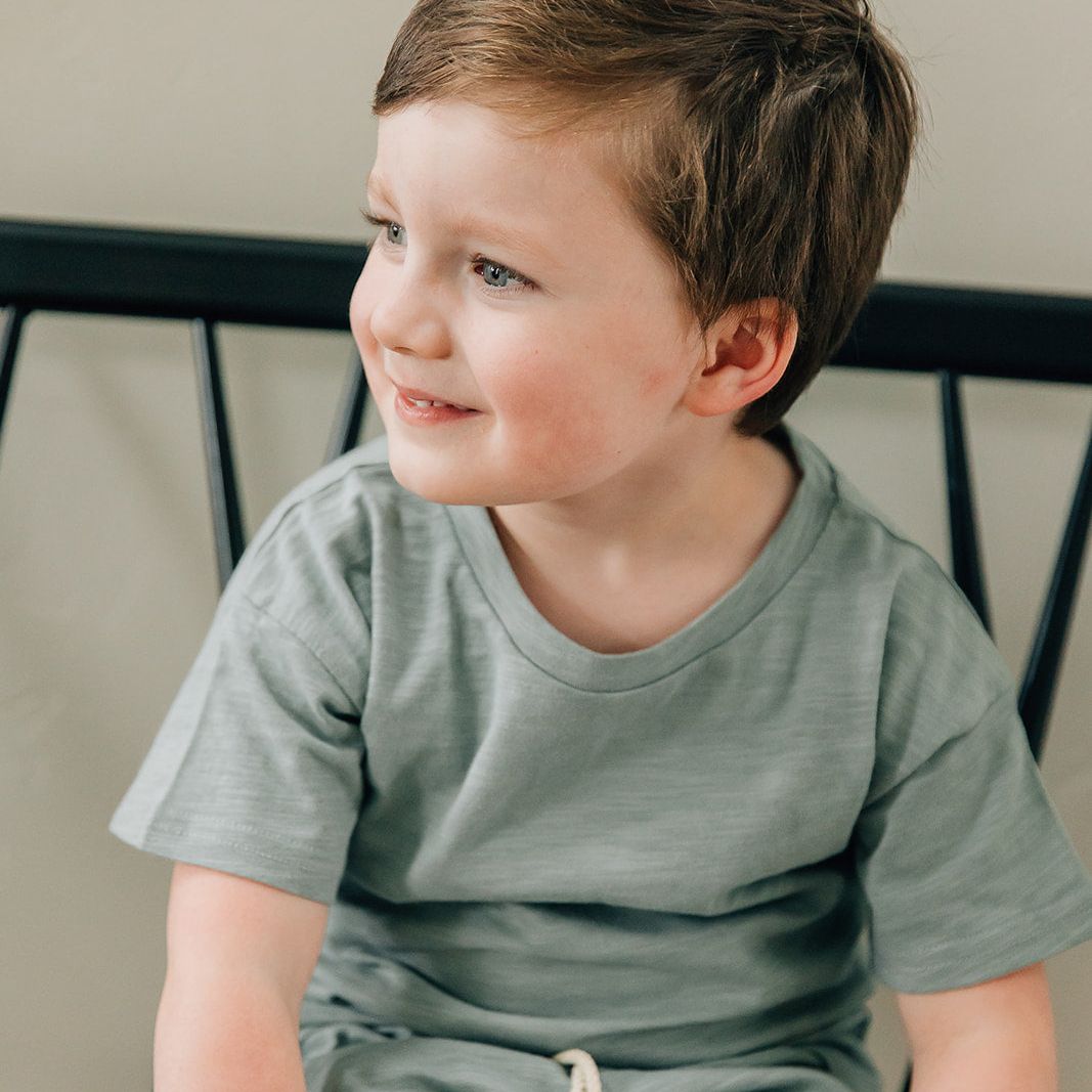 Young boy in a green shirt and shorts sitting on a chair.