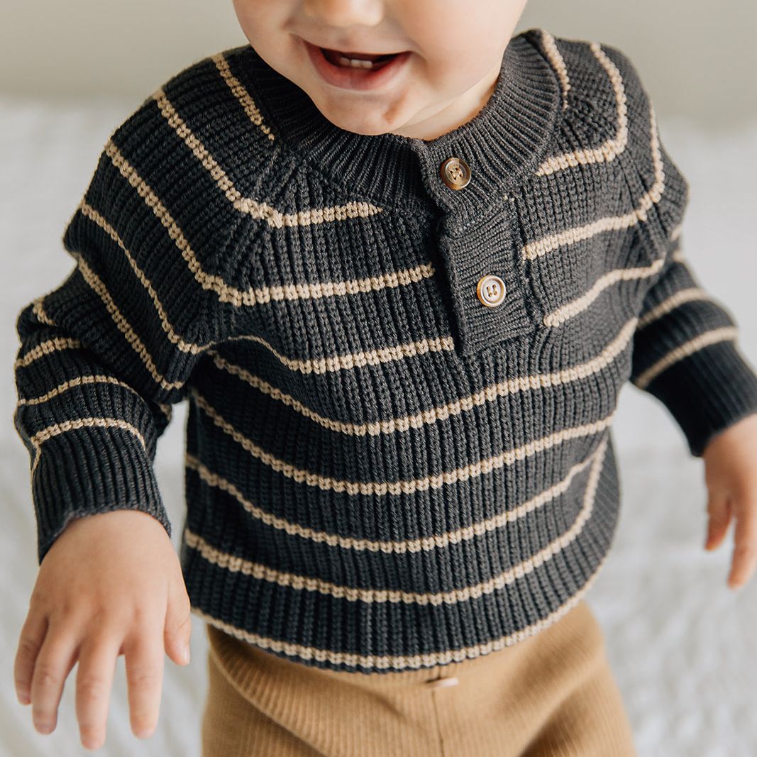 Child wearing a striped sweater and brown pants on a light background