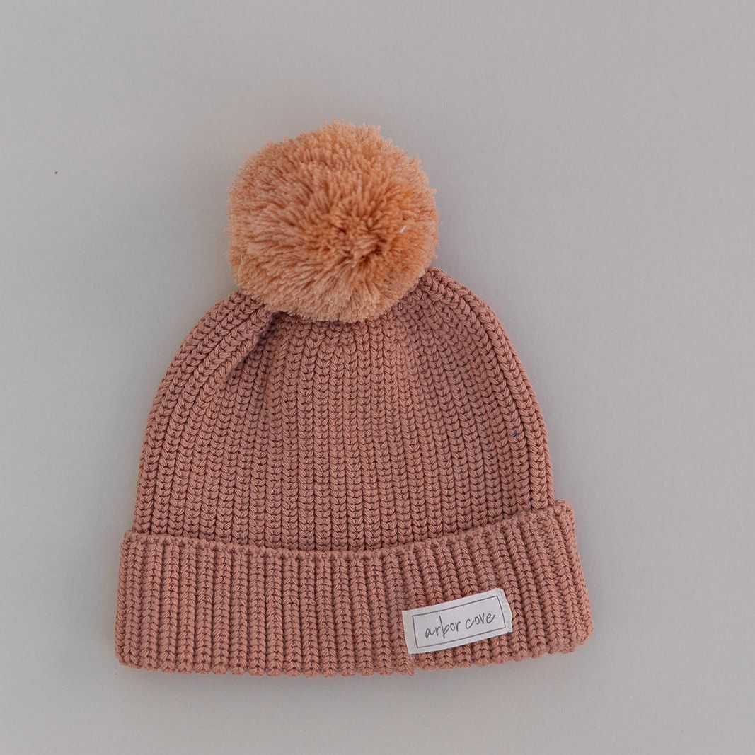 Rust colored baby Knitted beanie with a pom-pom on a plain background