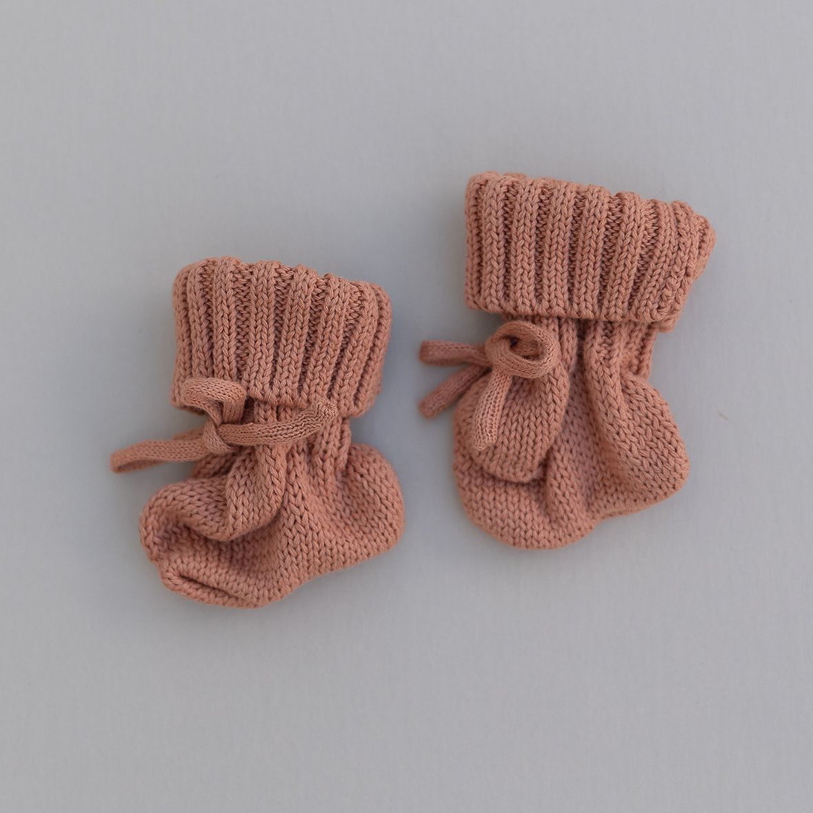 Pair of rust colored knitted baby booties on a gray background