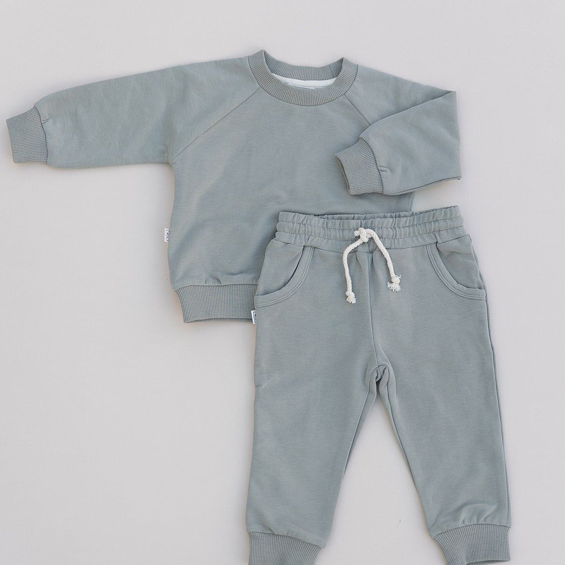 A baby jogger set in green, including a long-sleeved top and matching pants, laid flat on a white background.
