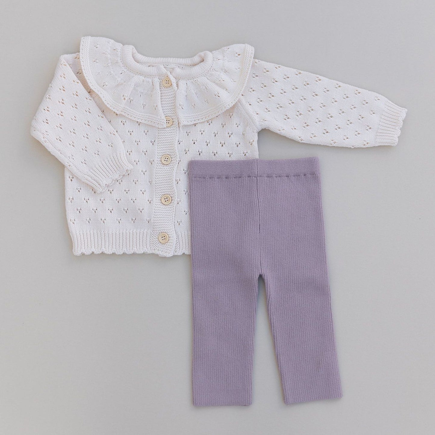 Cream cardigan with ruffled collar and purple leggings on a gray background