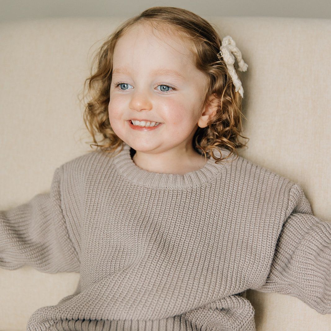 Child wearing a gray sweater sitting on a beige couch