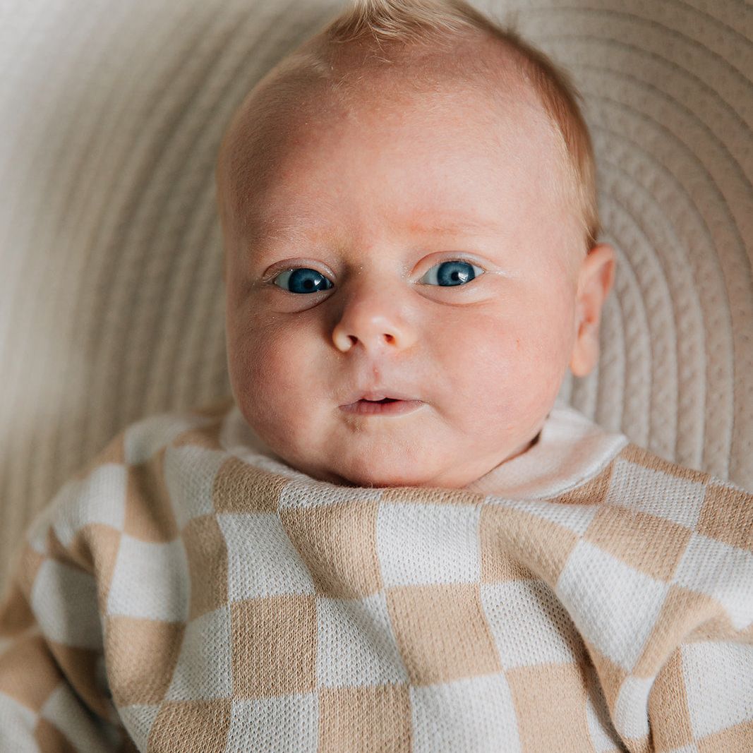Baby wearing a two-piece baby outfit with a checkered long-sleeve sweater in beige and white colors lying on a textured surface