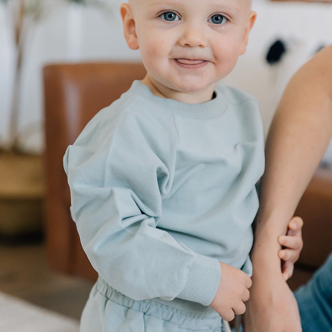 Child in a light blue jogger set standing indoors with a blurred background