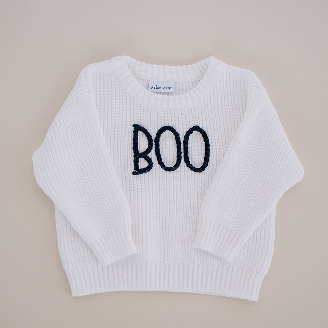 White organic cotton baby sweater with hand-stitched “BOO” lettering in black
