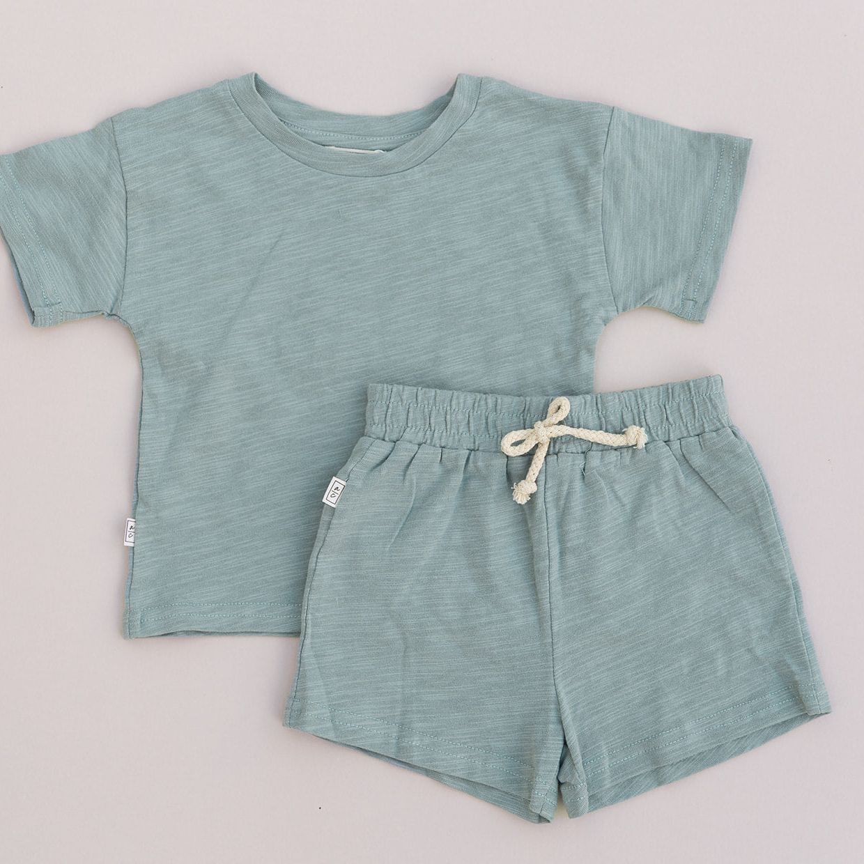 Green children's t-shirt and shorts set on a light gray background