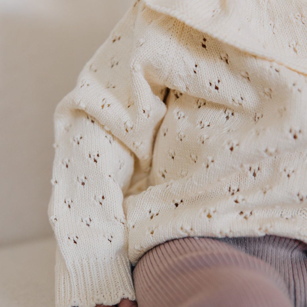 Close-up of a child wearing a cream-colored knitted pointelle sweater on a light background