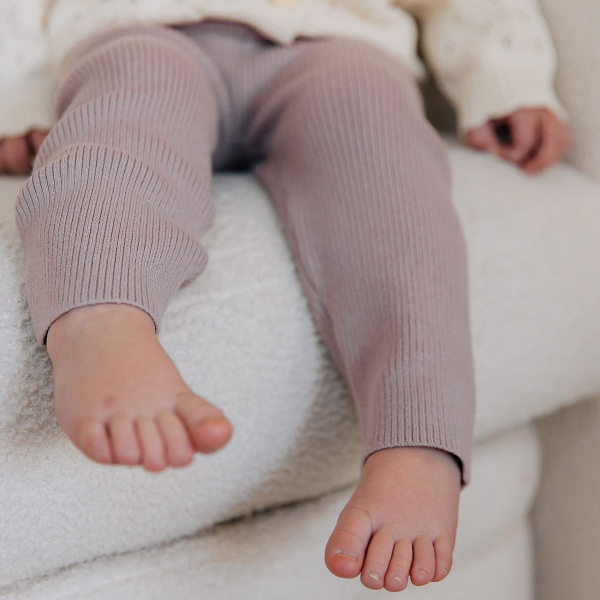 Child's legs wearing pink ribbed leggings on a white surface