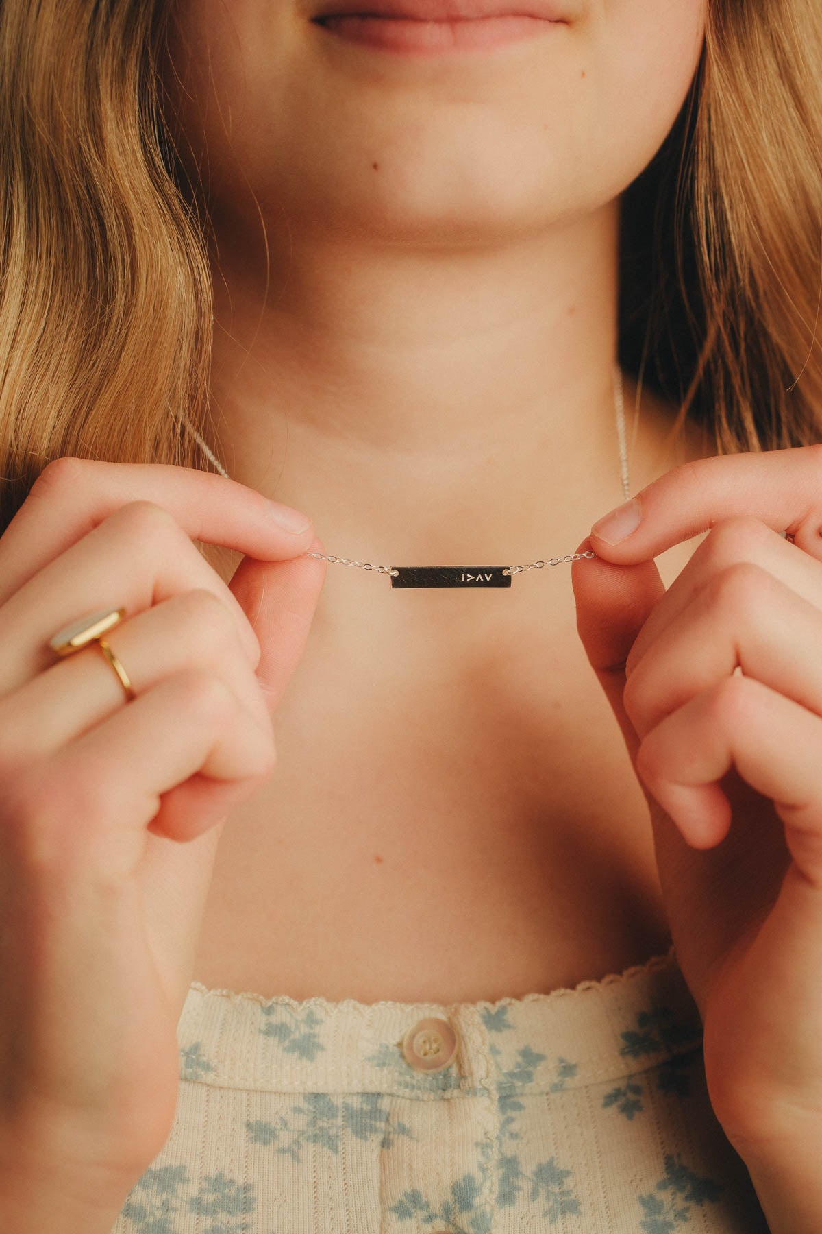 Person wearing a necklace with a nameplate with symbol I am greater than my highs and lows, held by hands.