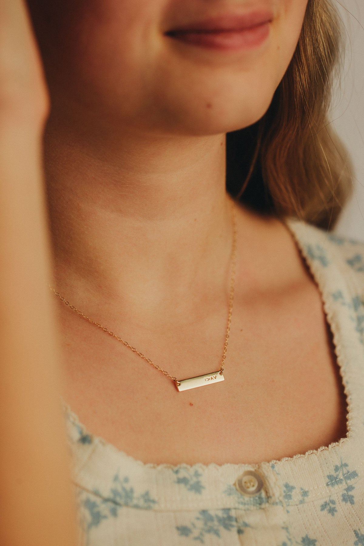 Close-up of a person wearing a gold necklace with a bar pendant with symbol I am greater than my highs and lows