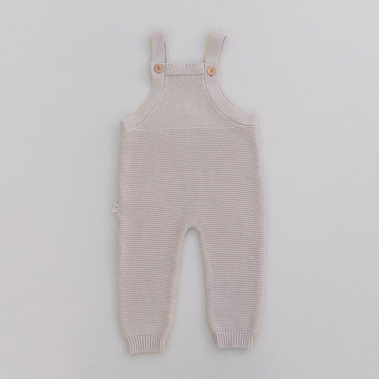 Knitted baby overalls in oat on a light gray background