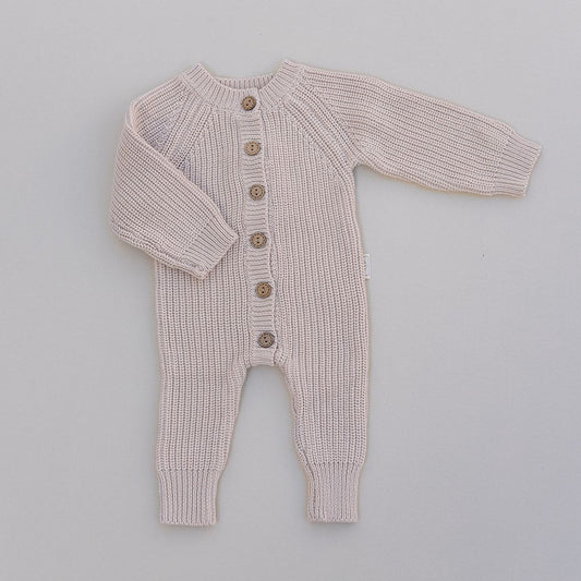 Knitted baby romper with buttons in cream on a light gray background