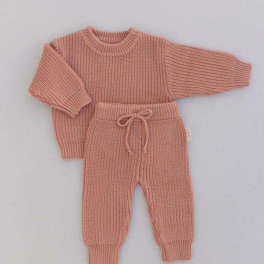 Knitted rust colored sweater and pants set on a gray background