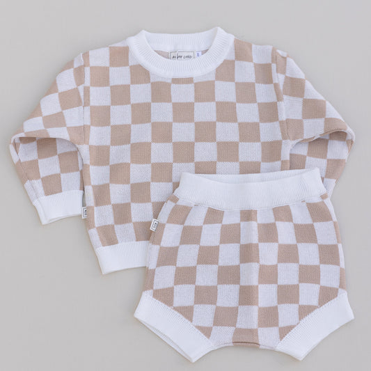 A two-piece baby outfit with a checkered long-sleeve sweater and matching bloomers in beige and white colors.