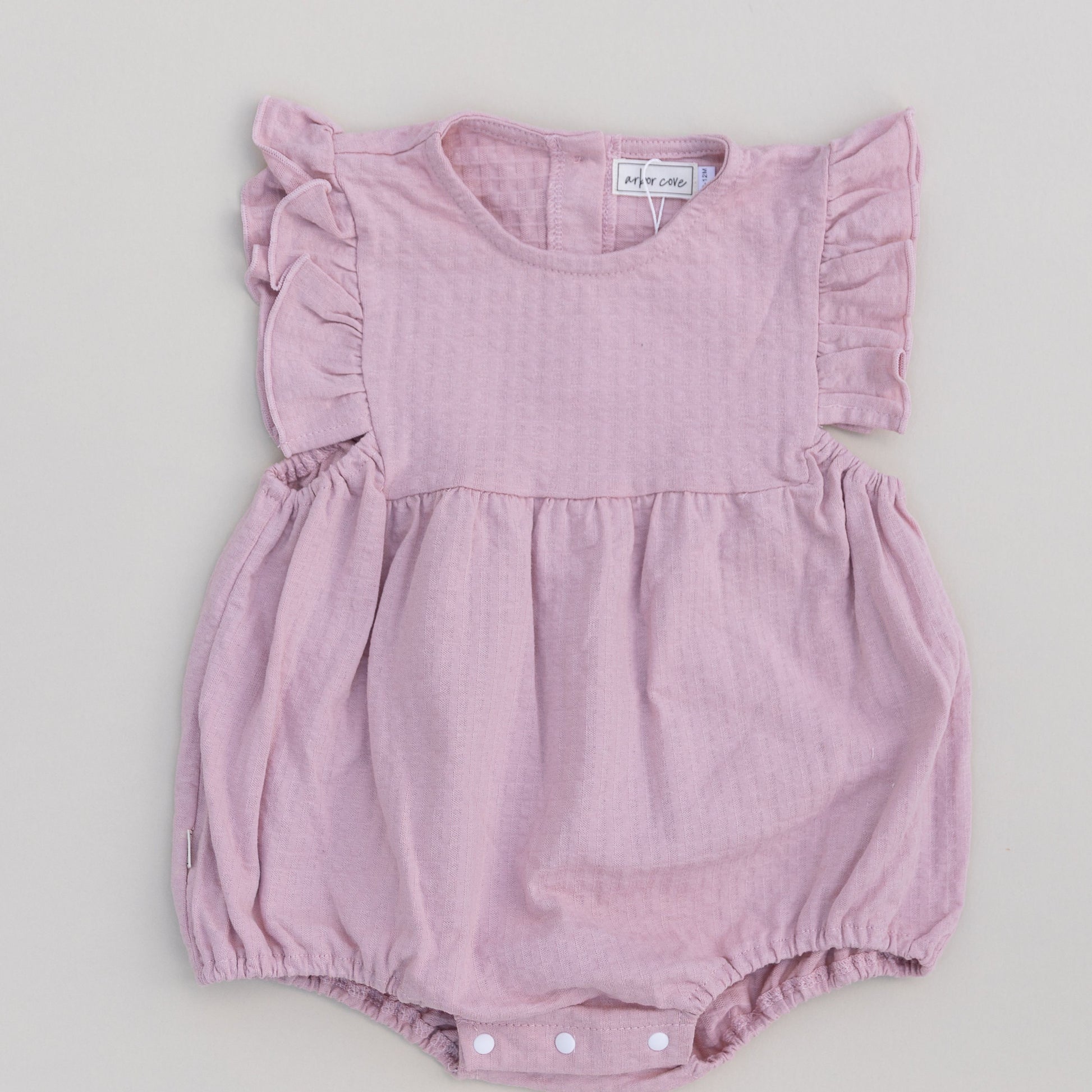A pink ruffled bubble onesie with short sleeves and snap closures on the bottom for a baby.