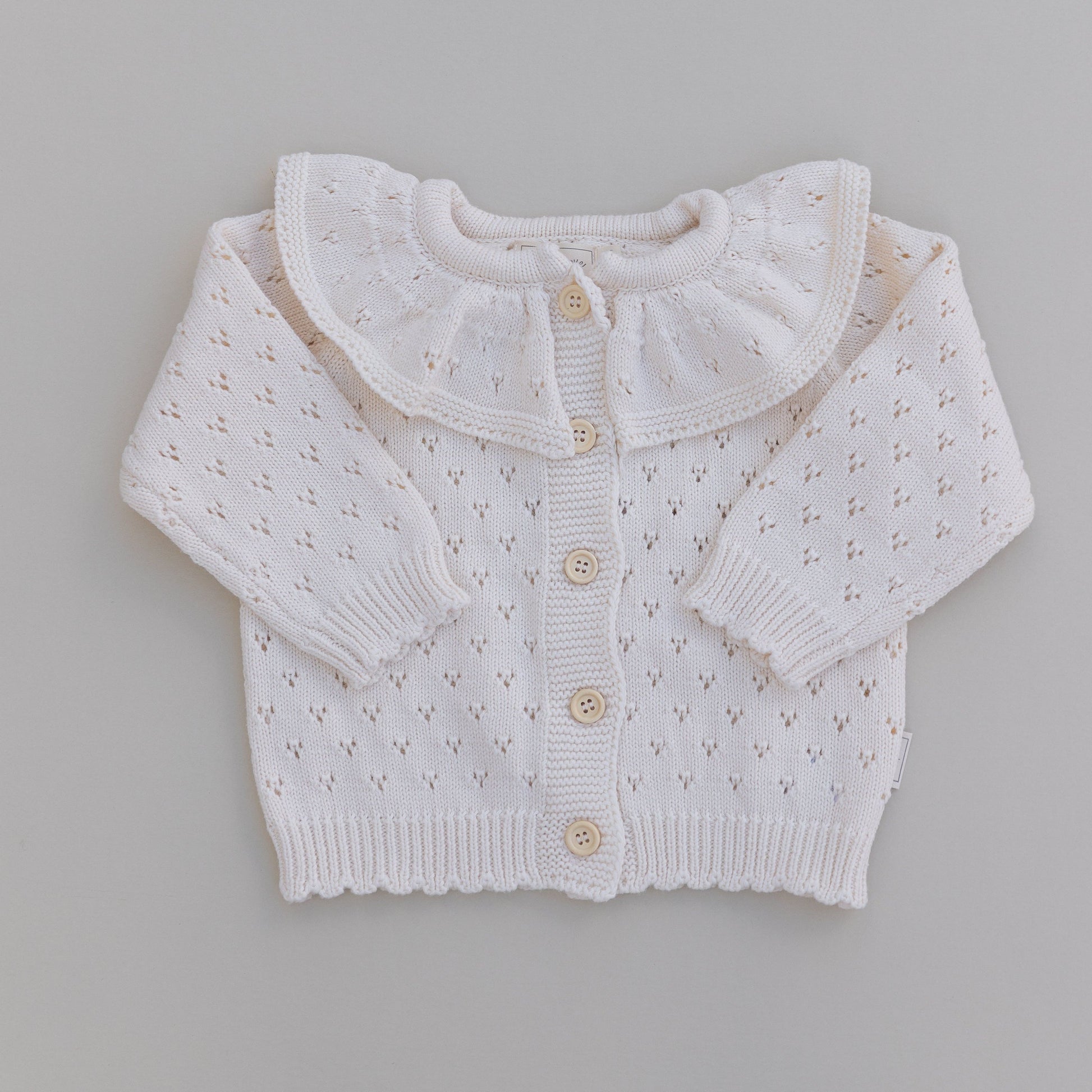 A cream ruffle neck pointelle cardigan with button-down front, laid flat on a neutral background.