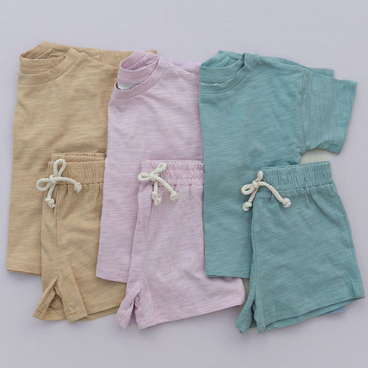 Three pairs of children's shorts in mustard, pink, green on a light gray background.